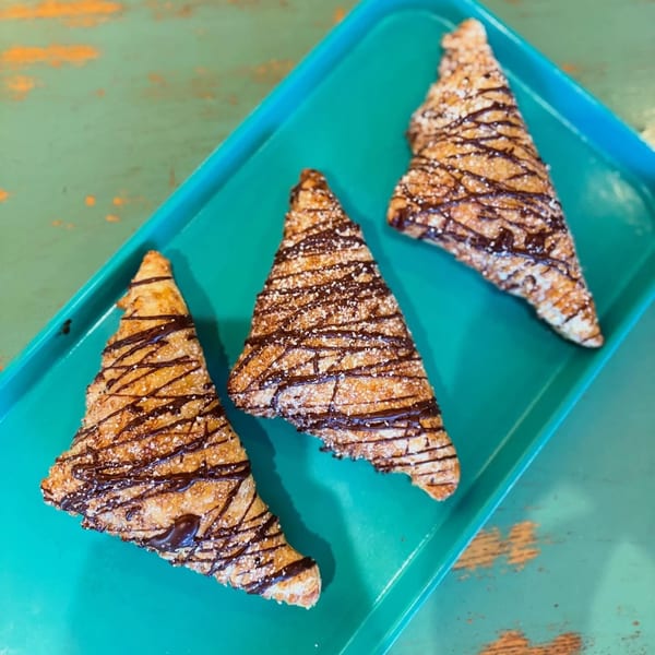 Three triangular pastries with chocolate drizzle and powdered sugar on a teal tray.