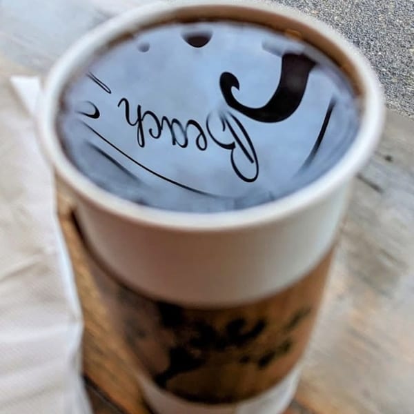 A cup of coffee with "Beach" reflected on its surface, sitting on a wooden table.